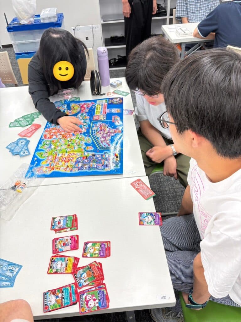 ボードゲームを三人の人が囲んでいる写真。